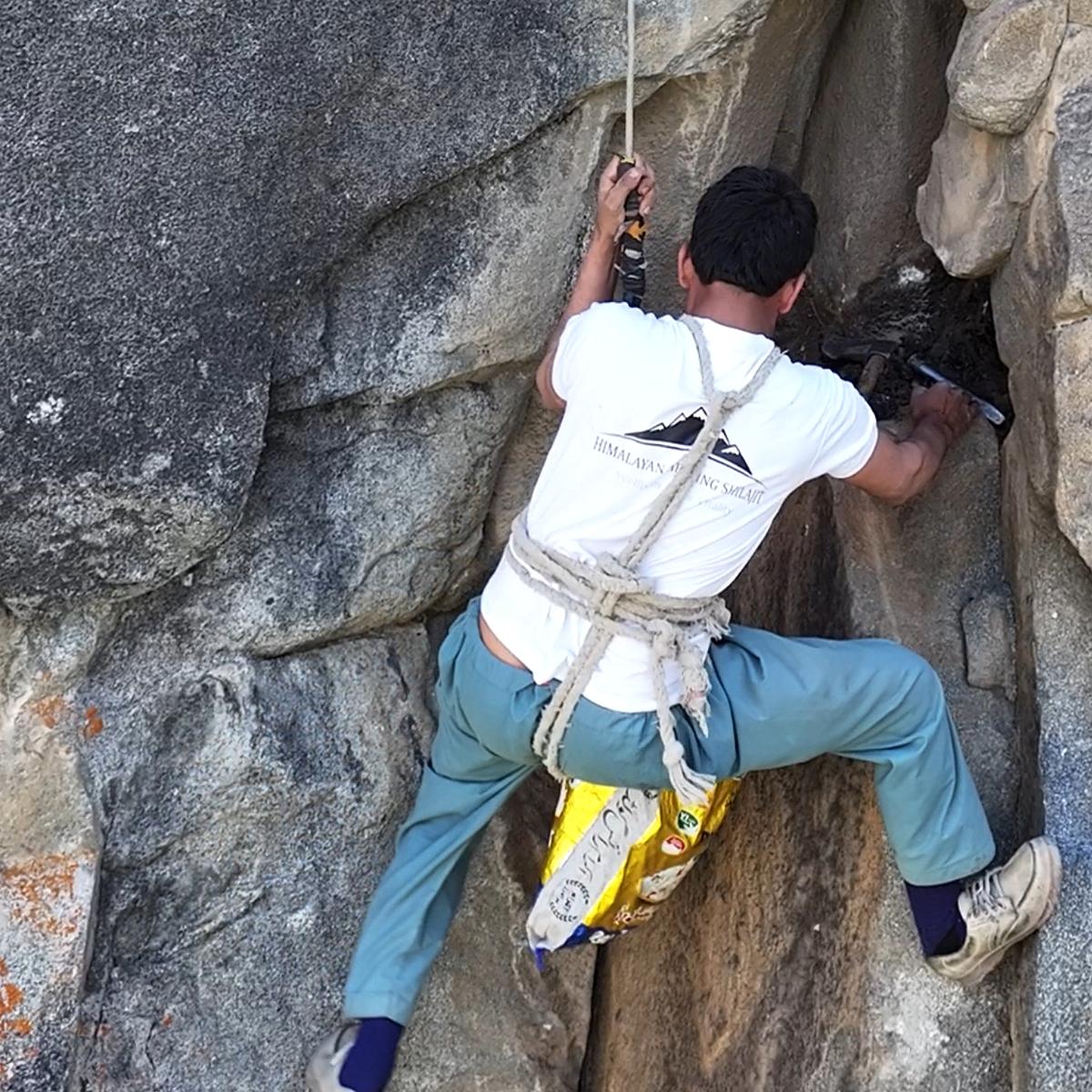 Shilajit collector roped onto a cliff face, extracting resin from a rock seam