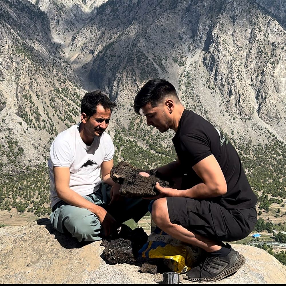 Two men examining and grading a raw shilajit rock by hand on a mountainside