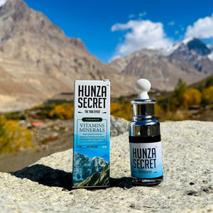 Hunza Secret shilajit drops: 50 ml box and glass dropper bottle on a rock in a Himalayan valley